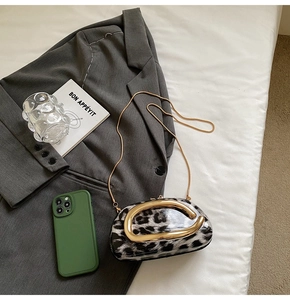 Detail of leopard print crossbody bag with large gold horseshoe handle on grey blazer