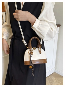 Detail of mini shell bag with brown trim, braided pendant and gold bell charm