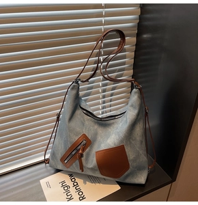 Detail of light blue washed canvas tote bag with brown leather straps and metal zipper pocket