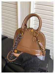 Détail du sac coquille marron brillant avec zips dorés et pendentif clochette rayé