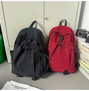 Close-up of textured nylon backpacks in black and brick red with drawstring pocket detail