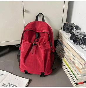 Detail of red checkered backpack featuring front drawstring pocket and mesh side compartment