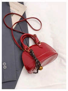 Vue détaillée du sac coquille rouge verni avec breloque cloche sur un blazer
