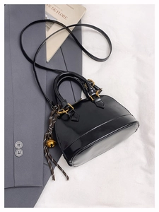 Détail du sac coquille noir verni avec finitions dorées et pendentif de clochette