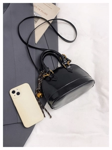 Détail d'un sac bandoulière noir brillant avec ferrures dorées et breloque cloche