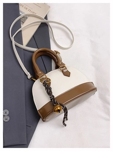 Détail du sac bandoulière bicolore avec breloque cloche sur fond de veste grise