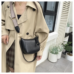 Detail of black crossbody bag with wide geometric strap and golden hardware accents