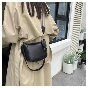 Detail of black leather crescent bucket bag with woven wide strap on khaki trench coat