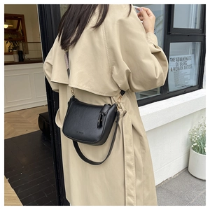 Detail view of black bucket bag with lychee texture and gold hardware on trench coat model