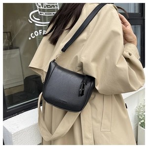 Detail of black wrinkled leather bag with fashion logo worn with a khaki trench coat