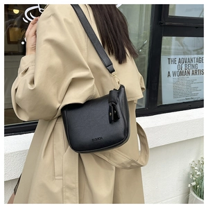 Close-up of black leather bucket bag with wide strap on a model in a beige coat