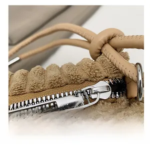 Détail du tissu peluche kaki avec fermeture éclair argentée et cordon en cuir cousu