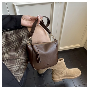 Detail of a brown leather saddle bag with wide shoulder strap worn by a model