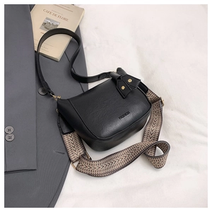 Macro detail of black leather bucket bag with fashion text and woven shoulder strap