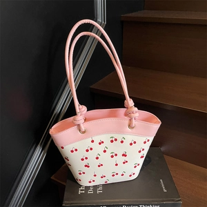 Pink and white bucket bag with cherry print and knot handles on a wooden staircase