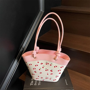 Contrast color bucket bag with cherry print and pink handles on a decorative background