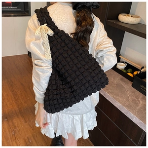 Detail of black bubble textured tote bag featuring a cream lace bow accent for women