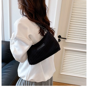 Détail du sac bandoulière en velours côtelé noir avec texture rainurée porté par le mannequin
