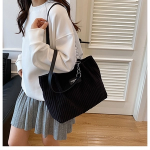 Detail of black corduroy tote bag showing chain strap and white fashion label on fabric