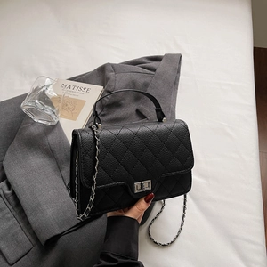 Détail de la texture cuir noir matelassé avec fermoir rotatif argenté et chaîne