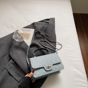 Détail du petit sac matelassé bleu clair avec fermoir argenté sur une veste grise