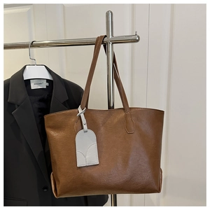 Detail of a brown PU leather tote bag with gray tag hanging on a metal hanger