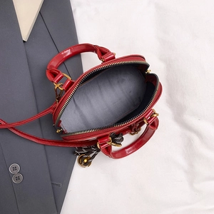 Sac coque élégant en cuir verni rouge avec détails dorés et breloque en nœud