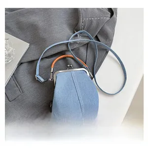 Close-up of vintage denim shell bag with bronze metal clasp on a grey blazer