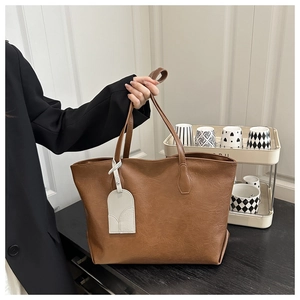 Close-up of brown textured leather tote bag with cream tag detail and dual handles