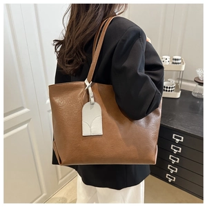 Close-up of brown leather tote bag with a white semi-circular tag charm on a model