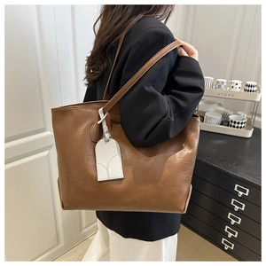 Detail of soft brown leather tote bag with white minimalist charm and textured finish