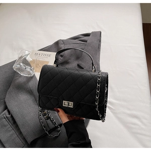 Detail of black quilted crossbody bag with silver clasp and chain on grey suit