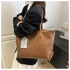 Detail view of large brown tote bag with textured litchi pattern and grey charm accessory