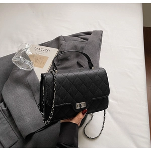 Détail du sac matelassé noir avec fermoir rotatif argenté et bandoulière en chaîne métal