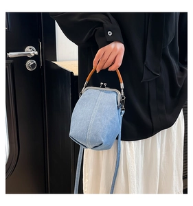 Detail of light blue denim shell bag with white stitching and brown leather handle