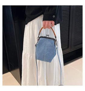 Detail of blue denim shell bag with brown leather handle and vintage metal clasp