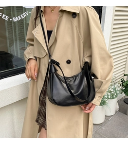 Detail of a black hobo crescent bag worn by a model in a beige trench coat