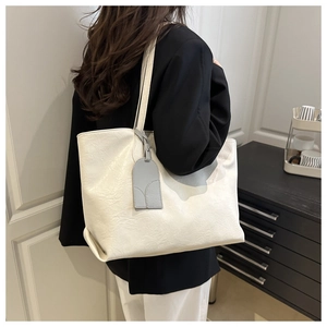 Detailed view of a creamy white tote bag with natural wrinkled texture and a gray charm