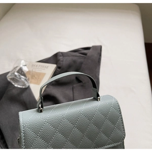 Détail du sac en cuir grainé bleu-vert clair avec rabat matelassé sur des draps blancs