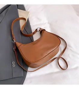 Close-up of brown leather dumpling bag on white fabric with stylish gray suit background