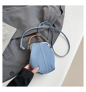 Detail of light blue denim shell bag with brown leather handle and metal clasp closure