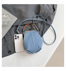 Detail of light blue denim bucket bag with metal kiss-lock closure and leather handle