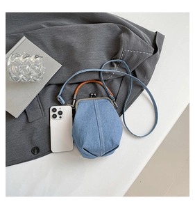 Top view of a denim bucket bag with brown leather handles next to a smartphone