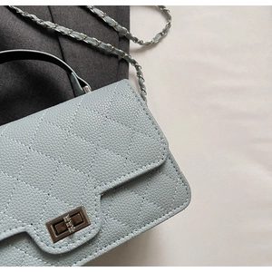 Détail macro du cuir matelassé bleu clair et du fermoir rotatif argenté du sac