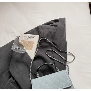 Détail du sac bandoulière matelassé bleu clair avec chaîne argentée sur drap blanc