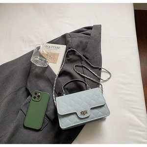 Sac bandoulière bleu clair matelassé avec chaîne et fermoir rotatif sur un blazer