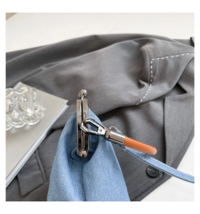 Detail of silver metal buckle and brown leather handle on blue denim bucket bag