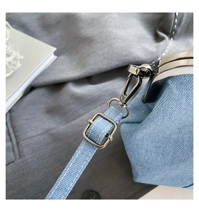 Macro detail of adjustable gunmetal buckle and white stitching on light blue denim bag