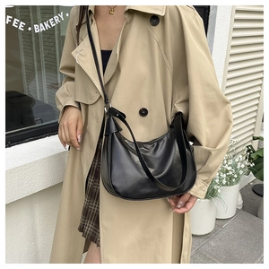 Detail of black matte leather hobo bag worn with a beige trench coat in a street style view