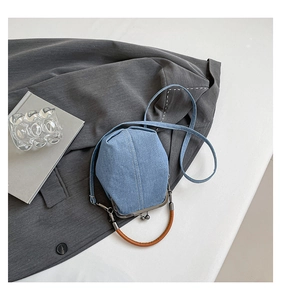 Detail of blue denim bucket bag with brown round handle and classic metal clasp closure